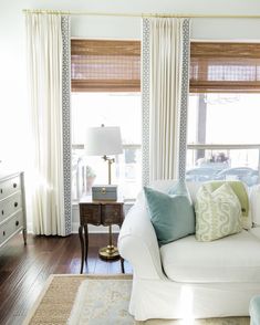 a living room with white couches and blue pillows on the sofa in front of two windows