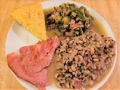 a white plate topped with meat and beans next to cornbread on top of a wooden table