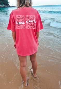 a woman is standing in the water at the beach wearing a pink shirt that says final fiesta