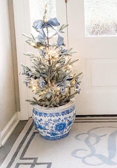 a small christmas tree in a blue and white pot on the floor next to a door