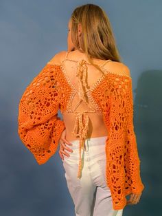 a woman wearing an orange crochet top and white pants with her back to the camera