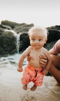 a man holding a baby on top of a sandy beach