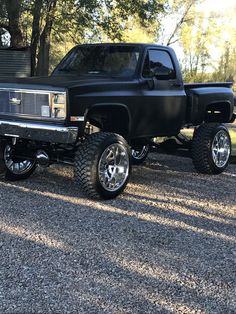 a black pickup truck parked on gravel with trees in the background