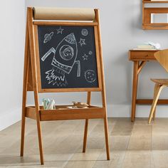 an easel with a chalkboard on it in front of a desk and chair