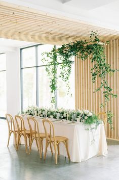 a long table with white flowers and greenery on it is surrounded by wooden chairs