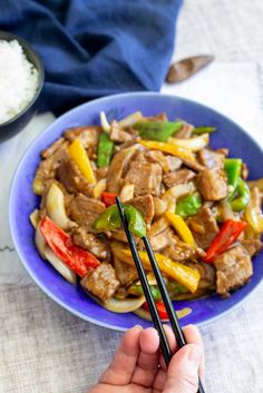 a person holding chopsticks over a plate of stir fry with meat and vegetables