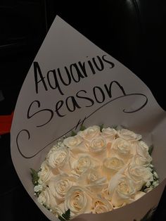 a bouquet of white roses sitting on top of a sign that says aquarius season