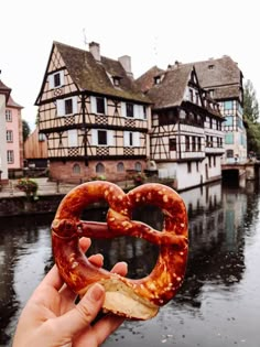 a person holding up a pretzel in front of some buildings on the water