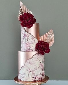 a three tiered cake decorated with pink and red flowers on a gold plated stand