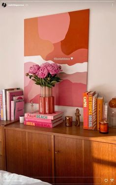 a vase with pink flowers on top of a wooden dresser next to books and magazines