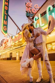 a man and woman kissing on the street in front of a building with neon signs