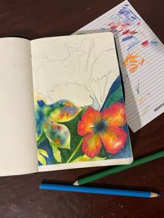 an open notebook with watercolors and pencils next to it on a table