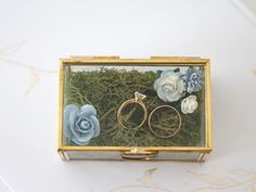 two wedding rings in a box with moss and flowers on the inside, sitting next to each other