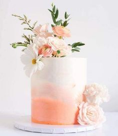 a white and pink ombreed cake with flowers on top is sitting on a plate