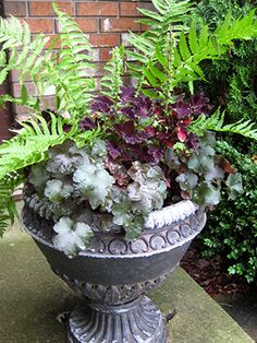 a planter filled with lots of green plants next to a brick wall and shrubbery