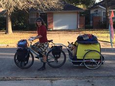 a woman is standing next to her bike with a dog in the sidecar and a trailer attached to it