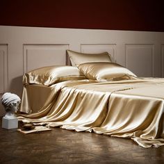 a bed with gold sheets and pillows on top of wooden flooring next to a white headboard