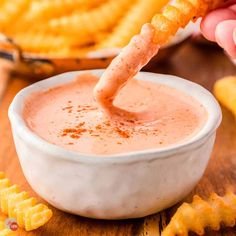 a person dipping some kind of sauce in a white bowl with cheetos on the side