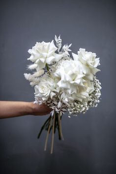 a bouquet of white flowers being held by a person's hand on a gray background