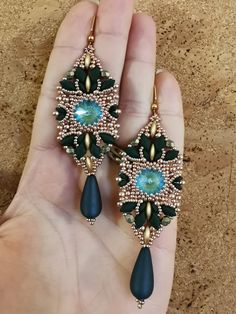 a pair of green and gold earrings in someone's hand