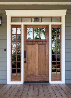 a wooden door on the side of a gray house with glass panes and windows