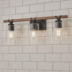 three light fixtures mounted on a white brick wall with wood beam and glass shade shades