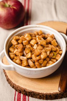 a white bowl filled with food on top of a wooden cutting board next to an apple