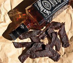 a bottle of whiskey sitting next to pieces of beef on top of a piece of paper