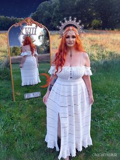 a woman with red hair wearing a white dress standing in front of a large mirror