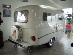 an old white trailer is parked in a room with tile flooring and large windows