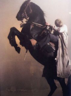 a man riding on the back of a black horse in foggy weather with an umbrella over his head