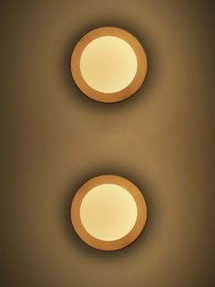 two circular lights are on the wall in front of a light brown background and one is white