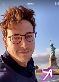 a man with glasses is smiling in front of the statue of liberty, and an arrow pointing up