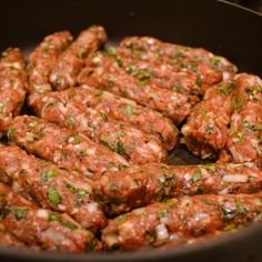 meatballs are cooking in a frying pan on the stove top, with herbs sprinkled all over them