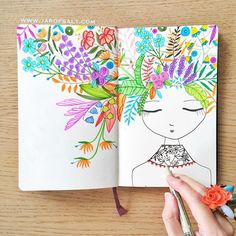 a person holding a pen and drawing flowers in a book