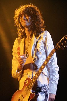 a man with long hair playing an electric guitar in front of a microphone on stage