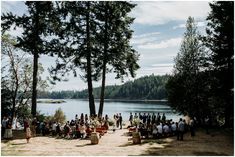 a group of people standing next to each other near a body of water with trees in the background