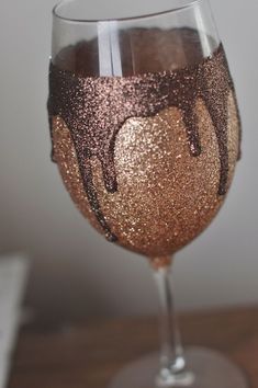 a wine glass filled with liquid on top of a wooden table next to a white wall