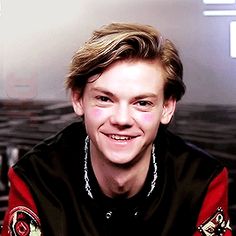 a young man is smiling and wearing a black, red and white jacket with patches on it