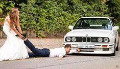 a bride and groom laying on the ground next to a white car