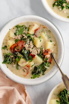 two bowls of soup with meat, potatoes and kale on the side next to a spoon