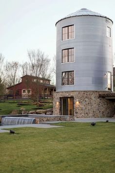 a round building with a waterfall in front of it on a grassy area next to buildings