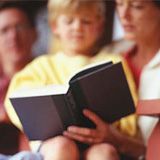 two children and an adult are sitting on a couch reading books together, while one child looks at the camera