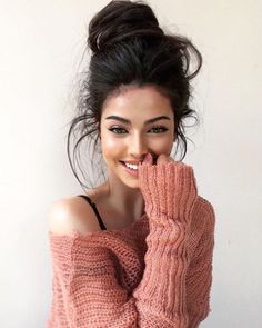 a woman with her hand on her face wearing a pink sweater and smiling at the camera