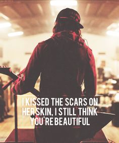 a person standing in front of a microphone with the words i kissed the scars on her skin, i still think you're beautiful