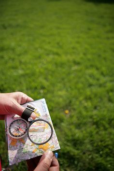 a person holding a compass and a map in their hand while looking at the grass