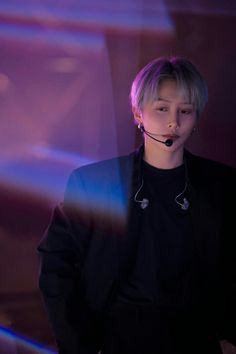 a young man wearing a black shirt and headphones standing in front of a purple background