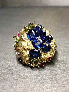 A colorful cocktail ring crafted in deep 18K yellow, gold and set with approximately 7.50cttw in oval buff top blue sapphires as well as round yellow and pink sapphires as well as green marquise shaped sapphires and .15cttw in G-I color Vs1-2 clarity round diamonds. Dimensions/Weight: Ring measures .90" in diameter and weighs 13.9g. Size 7.5 (sizable). Condition: All stones are secure and in perfectly wearable condition. R-BCCL Luxury Gold Sapphire Ring Collectible, Luxury Gold Multi-stone Sapphire Ring, Multicolor Sapphire Multi-stone Ring, Multicolor Multi-stone Sapphire Ring, Multicolor Sapphire Ring In Fine Jewelry Style, Multicolor Oval Sapphire Ring For Formal Occasions, Oval Multicolor Sapphire Ring For Formal Occasions, Multicolor Oval Sapphire Ring, Oval Blue Multi-stone Sapphire Ring