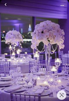 the tables are set with candles and centerpieces for an elegant wedding reception in purple lighting