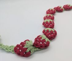 a crocheted necklace with red and green beads is displayed on a white surface